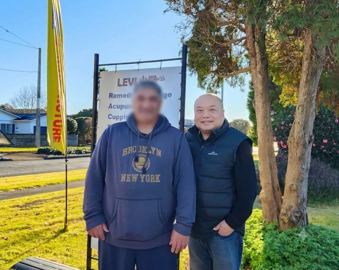 Mr B standing outdoors with Levi beside the clinic sign
